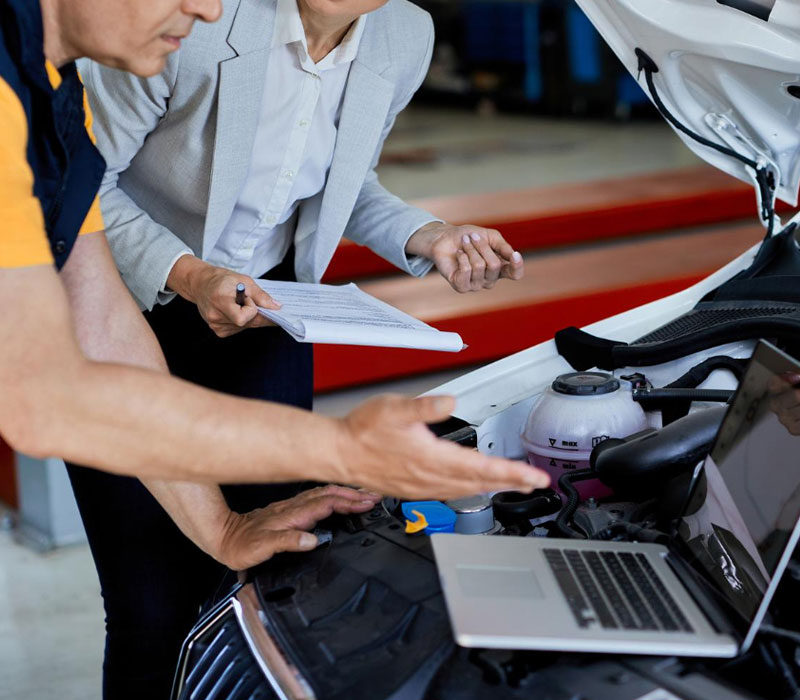 Perito y mecánico revisando el motor de un coche en un taller.